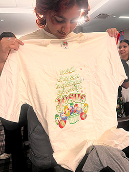 My friend holding up a white t-shirt that reads 'I put all of my eggs in one basket and gave it to Jesus'.