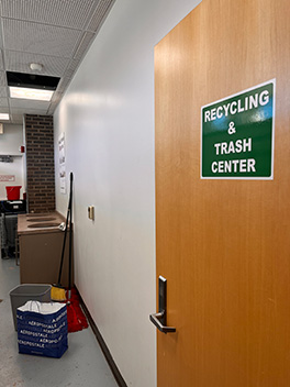 An open door with a 'Recycling and Trash Center' sign leading to a garbage room.